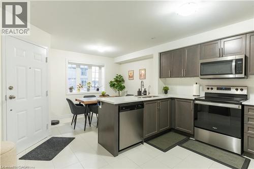 Kitchen with appliances with stainless steel finishes, a peninsula, dark brown cabinets, backsplash, and light tile patterned flooring - 85 Mullin Drive Unit# 20B, Guelph, ON - Indoor Photo Showing Kitchen