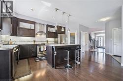 Kitchen with wall chimney range hood, appliances with stainless steel finishes, backsplash, dark wood-style flooring, and a center island - 