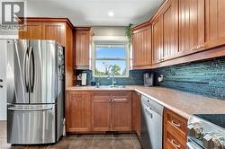 Kitchen featuring appliances with stainless steel finishes, tasteful backsplash, brown cabinets, light countertops, and dark tile patterned floors - 