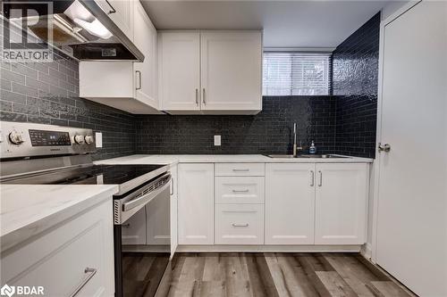 Kitchen with stainless steel electric range, decorative backsplash, custom exhaust hood, white cabinets, and light wood-style floors - 22 St James Street Unit# C, Brantford, ON - Indoor Photo Showing Kitchen