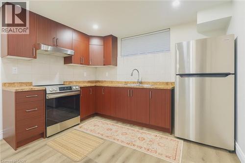 Kitchen with appliances with stainless steel finishes, under cabinet range hood, light wood finished floors, and decorative backsplash - 19 Sassafras Street Unit# Lower, Kitchener, ON - Indoor Photo Showing Kitchen