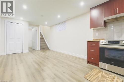 Kitchen featuring stainless steel range oven, light wood-style floors, under cabinet range hood, decorative backsplash, and light stone countertops - 19 Sassafras Street Unit# Lower, Kitchener, ON - Indoor Photo Showing Kitchen
