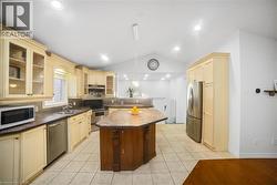 Kitchen featuring vaulted ceiling, appliances with stainless steel finishes, light tile patterned floors, dark countertops, and a center island - 