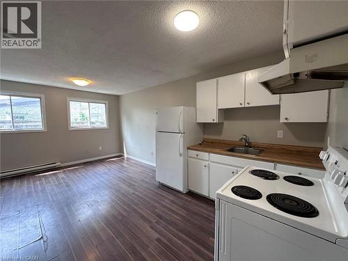 Kitchen featuring white appliances, white cabinets, a textured ceiling, under cabinet range hood, and dark wood-type flooring - 17 St Leger Street, Kitchener, ON - Indoor Photo Showing Kitchen