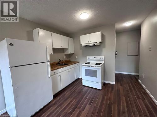 Kitchen featuring white appliances, white cabinetry, a textured ceiling, dark wood-type flooring, and under cabinet range hood - 17 St Leger Street, Kitchener, ON - Indoor Photo Showing Kitchen