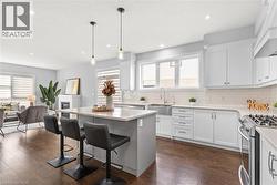 Kitchen featuring gas range, hanging light fixtures, white cabinetry, dark wood-type flooring, and custom exhaust hood - 