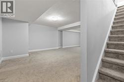 Finished below grade area with stairway, light colored carpet, and a textured ceiling - 