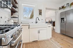 Kitchen featuring open shelves, appliances with stainless steel finishes, light wood-style floors, decorative backsplash, and white cabinetry - 