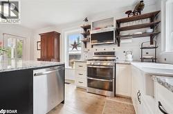Kitchen with stainless steel appliances, light stone counters, white cabinetry, plenty of natural light, and ornamental molding - 