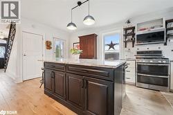 Kitchen with stainless steel appliances, light stone counters, pendant lighting, light wood finished floors, and crown molding - 