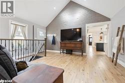 Living area featuring high vaulted ceiling, light wood-style flooring, and brick wall - 