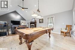 Playroom featuring light wood-style floors, billiards table, a fireplace, a ceiling fan, and high vaulted ceiling - 