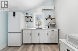Bar area with white cabinetry, open shelves, white appliances, light wood-type flooring, and vaulted ceiling - 