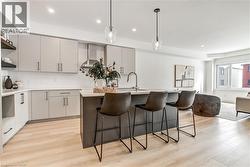 Kitchen with hanging light fixtures, open shelves, an island with sink, light wood-type flooring, and decorative backsplash - 