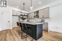 Kitchen with gray cabinets, a breakfast bar area, decorative light fixtures, wall chimney range hood, and recessed lighting - 