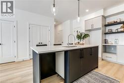 Kitchen with open shelves, light wood-type flooring, hanging light fixtures, modern cabinets, and a center island with sink - 