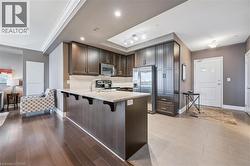 Kitchen with stainless steel appliances, dark brown cabinetry, a peninsula, light stone counters, and ornamental molding - 