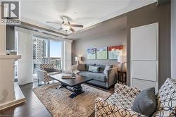 Living room featuring dark wood-style flooring, ornamental molding, ceiling fan, and a premium fireplace - 