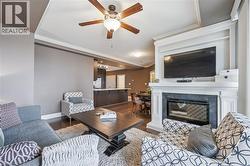 Living area featuring ornamental molding, dark wood-style flooring, a premium fireplace, and ceiling fan - 