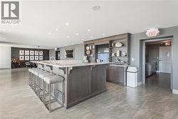 Kitchen with a breakfast bar, dark brown cabinets, light stone counters, a large island with sink, and open shelves - 