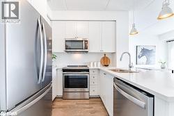 Kitchen featuring appliances with stainless steel finishes, tasteful backsplash, white cabinetry, a peninsula, and decorative light fixtures - 