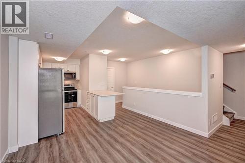 Kitchen featuring appliances with stainless steel finishes, white cabinets, light countertops, a textured ceiling, and light wood-style floors - 118 Gravel Ridge Trail Unit# C17, Kitchener, ON - Indoor Photo Showing Kitchen