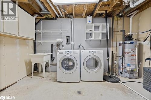 Laundry room featuring concrete flooring, washing machine and dryer, water heater, and cabinet space - 16 Bush Street, Collingwood, ON - Indoor Photo Showing Laundry Room