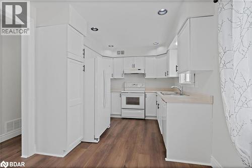 Kitchen with white appliances, light countertops, white cabinets, dark wood finished floors, and under cabinet range hood - 16 Bush Street, Collingwood, ON - Indoor Photo Showing Kitchen With Double Sink