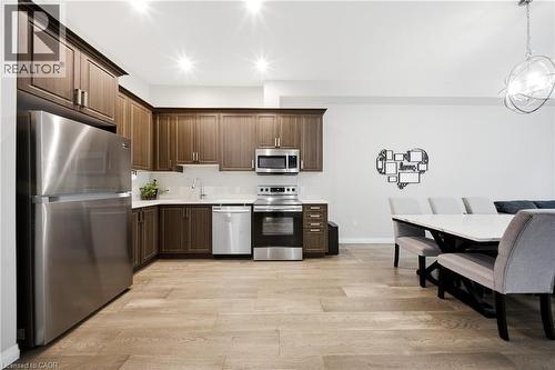 Kitchen featuring appliances with stainless steel finishes, light wood finished floors, dark brown cabinets, and hanging light fixtures - 85 Morrell Street Unit# 102A, Brantford, ON - Indoor Photo Showing Kitchen