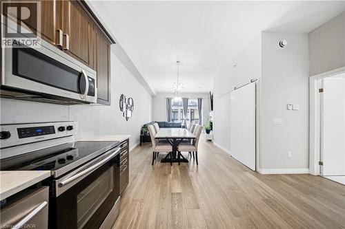 Kitchen featuring appliances with stainless steel finishes, light wood-style flooring, pendant lighting, and open floor plan - 85 Morrell Street Unit# 102A, Brantford, ON - Indoor Photo Showing Kitchen