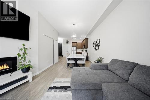 Living area with a warm lit fireplace, light wood-style floors, and a chandelier - 85 Morrell Street Unit# 102A, Brantford, ON - Indoor Photo Showing Living Room With Fireplace