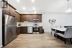 Kitchen featuring appliances with stainless steel finishes, light wood finished floors, dark brown cabinets, and hanging light fixtures - 