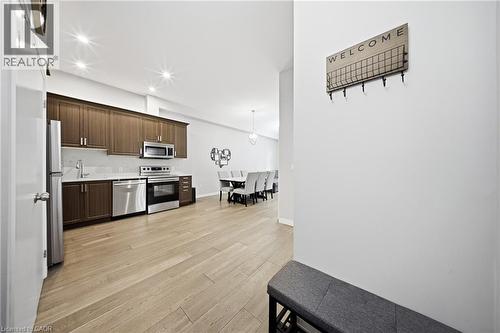 Kitchen with appliances with stainless steel finishes, dark brown cabinetry, hanging light fixtures, light wood-style flooring, and recessed lighting - 85 Morrell Street Unit# 102A, Brantford, ON - Indoor Photo Showing Kitchen