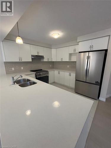 Kitchen featuring appliances with stainless steel finishes, tasteful backsplash, hanging light fixtures, white cabinetry, and under cabinet range hood - 12 Riddell Drive, Stratford, ON - Indoor Photo Showing Kitchen With Double Sink