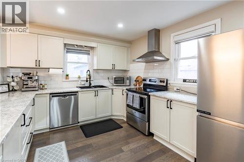 Kitchen featuring appliances with stainless steel finishes, wall chimney exhaust hood, dark wood-style floors, white cabinetry, and light stone countertops - 266 Melrose Avenue, Kitchener, ON - Indoor Photo Showing Kitchen With Double Sink With Upgraded Kitchen
