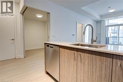 Kitchen featuring light stone countertops, stainless steel dishwasher, light wood finished floors, and light brown cabinetry - 