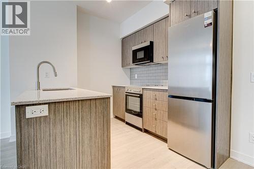 Kitchen featuring stainless steel appliances, light stone counters, tasteful backsplash, and light wood-type flooring - 25 Wellington Street A S Unit# 209, Kitchener, ON - Indoor Photo Showing Kitchen