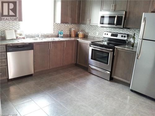 Kitchen featuring appliances with stainless steel finishes, decorative backsplash, light tile patterned floors, and light countertops - 55 Mooregate Crescent Unit# 3, Kitchener, ON - Indoor Photo Showing Kitchen