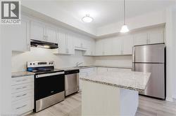 Kitchen with light wood-type flooring, light stone counters, under cabinet range hood, stainless steel appliances, and a sink - 