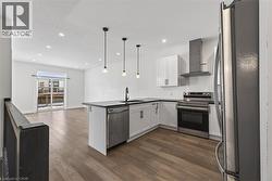 Kitchen with stainless steel appliances, wall chimney range hood, a peninsula, open floor plan, and white cabinetry - 