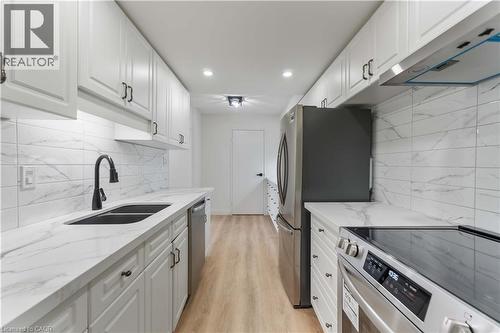 Kitchen featuring stainless steel appliances, ventilation hood, white cabinets, light stone counters, and backsplash - 120 Duke Street Unit# 905, Hamilton, ON - Indoor Photo Showing Kitchen With Double Sink With Upgraded Kitchen