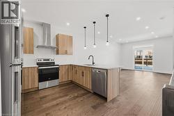 Kitchen featuring appliances with stainless steel finishes, open floor plan, wall chimney range hood, hanging light fixtures, and recessed lighting - 