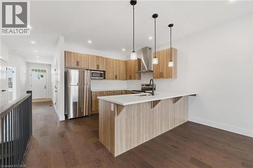 Kitchen with appliances with stainless steel finishes, a breakfast bar area, a peninsula, wall chimney range hood, and dark wood finished floors - 4 Elgin Street W, Norwich, ON - Indoor Photo Showing Kitchen With Stainless Steel Kitchen With Double Sink With Upgraded Kitchen