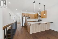 Kitchen featuring a breakfast bar, stainless steel appliances, wall chimney range hood, a peninsula, and dark wood-type flooring - 