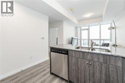 Kitchen with open floor plan, dishwasher, light stone countertops, light wood-type flooring, and a tray ceiling - 