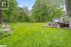 View of grassy yard featuring a patio area, view of wooded area, an outdoor structure, and an outdoor living space - 