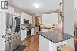 Kitchen featuring stainless steel appliances, white cabinets, a peninsula, dark wood finished floors, and dark stone countertops - 