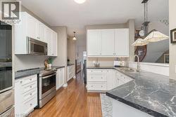 Kitchen with stainless steel appliances, pendant lighting, white cabinets, and dark wood-type flooring - 