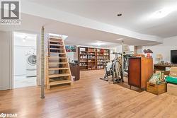 Finished below grade area with light wood-style flooring, stairs, and washer / dryer - 