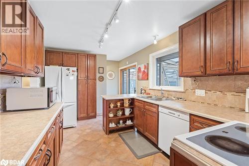 Kitchen with backsplash, brown cabinetry, white appliances, light countertops, and track lighting - 11317 Regional Road 25, Halton Hills, ON - Indoor Photo Showing Kitchen With Double Sink